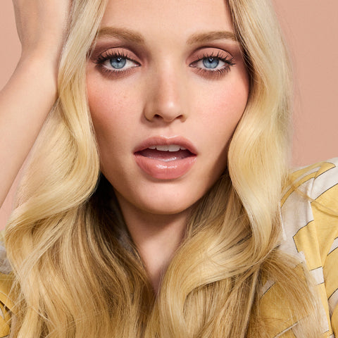 Close-up of a person with blonde hair and blue eyes against a pink background