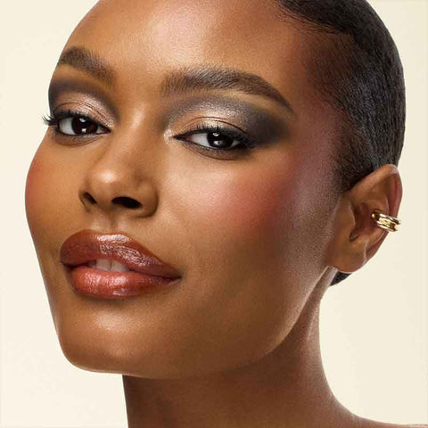 Close-up of a woman's face with makeup and an earring on a beige background